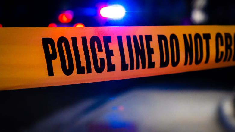 Police tape stretching across a road in front of a crime scene.