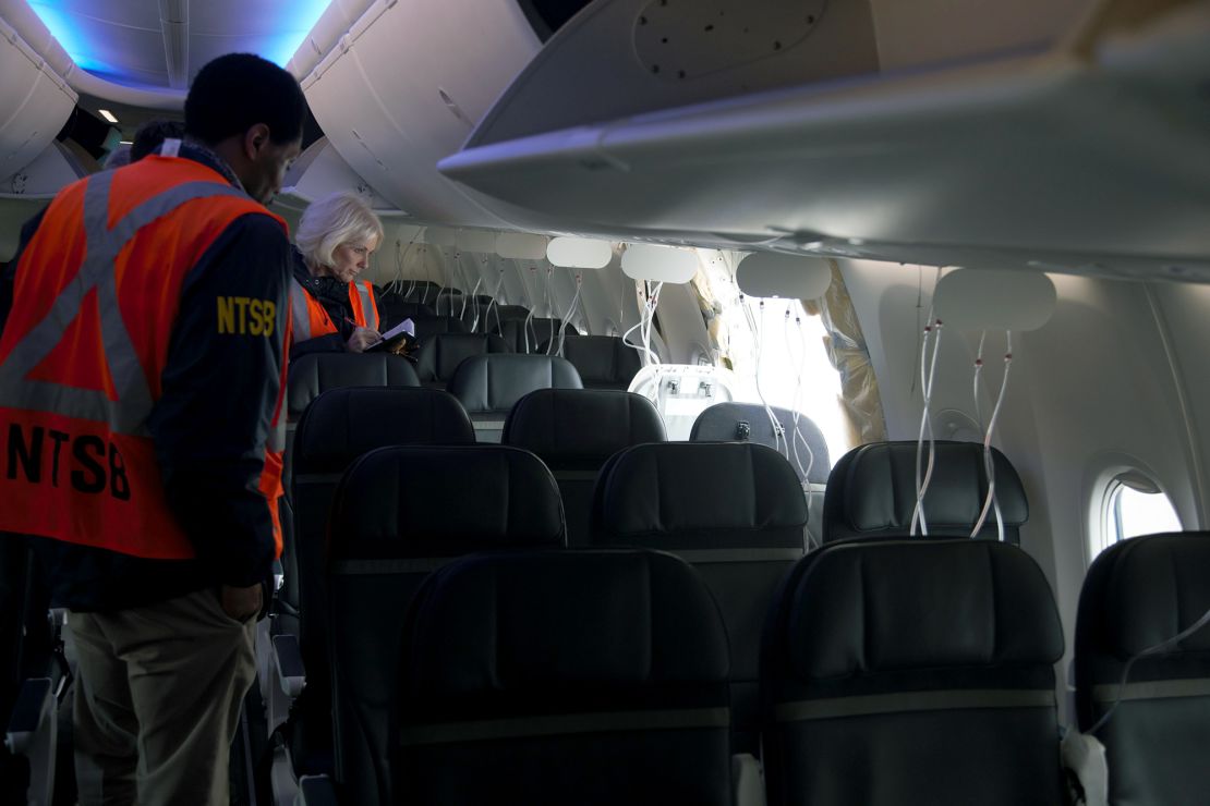 In this National Transportation Safety Board (NTSB) handout, members of the NTSB examine the hole in the fuselage plug area of Alaska Airlines Flight 1282 Boeing 737-9 MAX on January 7, 2024 in Portland, Oregon, two days after the flight in which it blew off in flight.