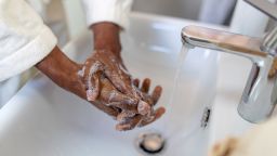 Close-up of a person lathering hands with soap and water over a bathroom sink, promoting hygiene and health.