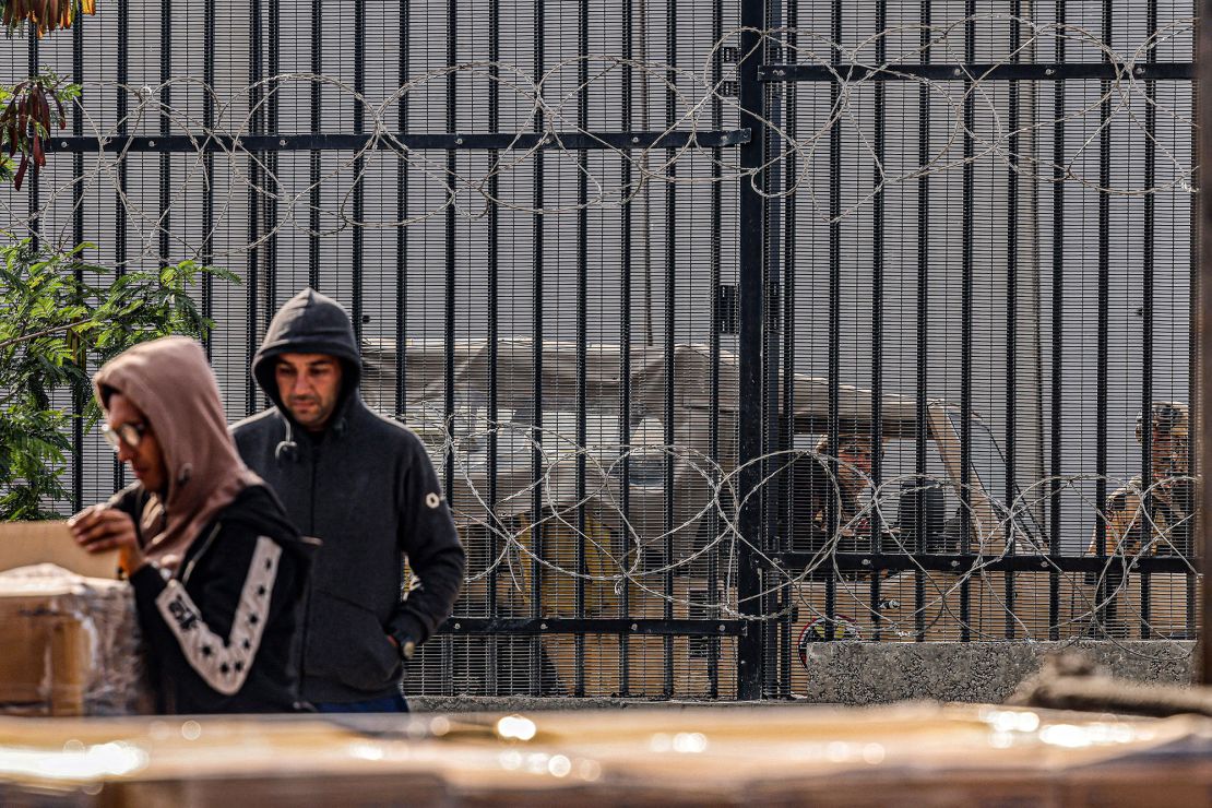 Egyptian army soldiers look on from behind the barbed-wire border fence as Palestinian workers unload crates of humanitarian aid entering the Gaza Strip through the Kerem Shalom (Karm Abu Salem) border crossing in the southern part of the enclave on January 29.