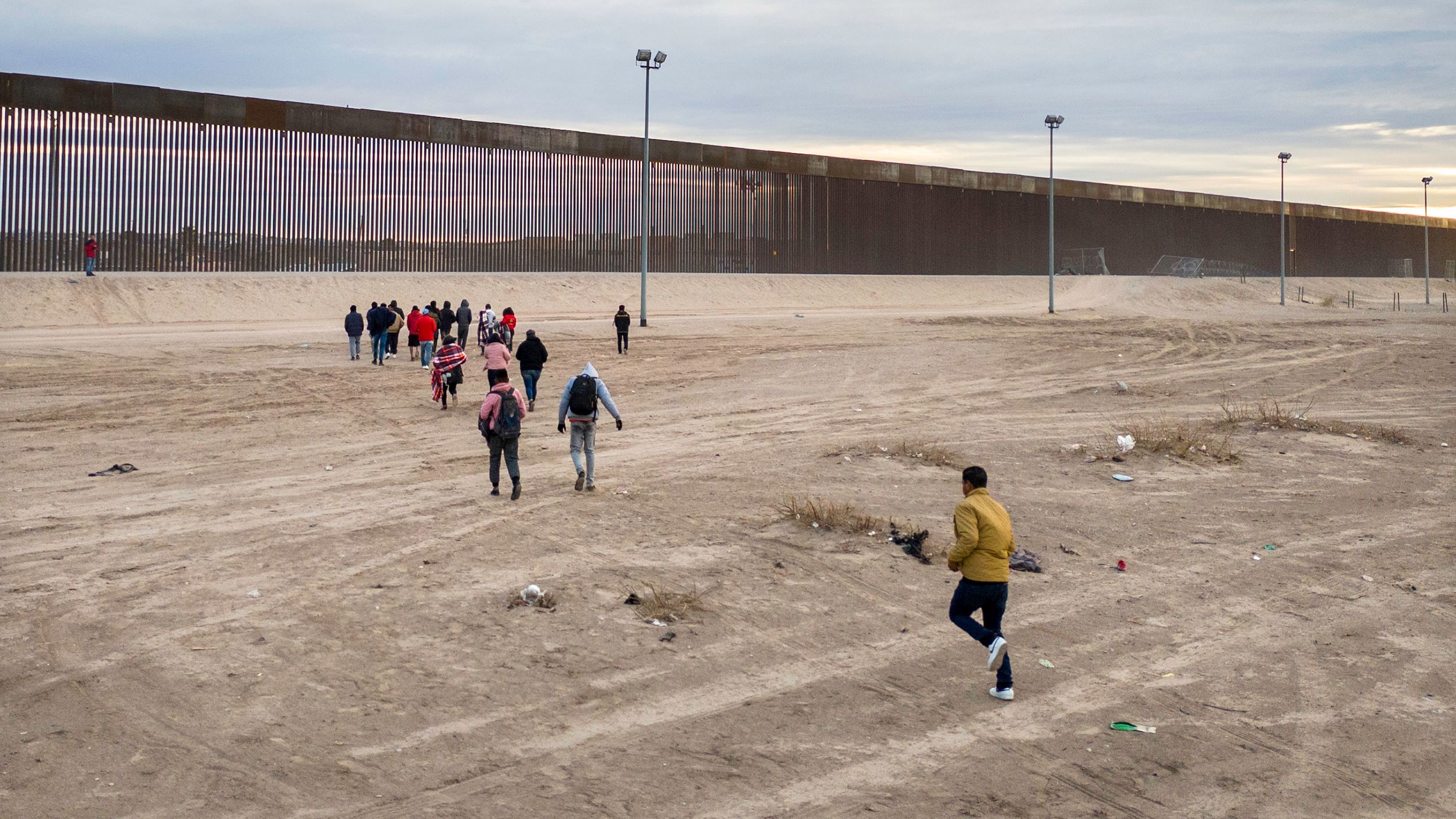Immigrants run towards the US-Mexico border wall after crossing the Rio Grande into El Paso, Texas, on February 1, 2024, from Ciudad Juarez, Mexico.