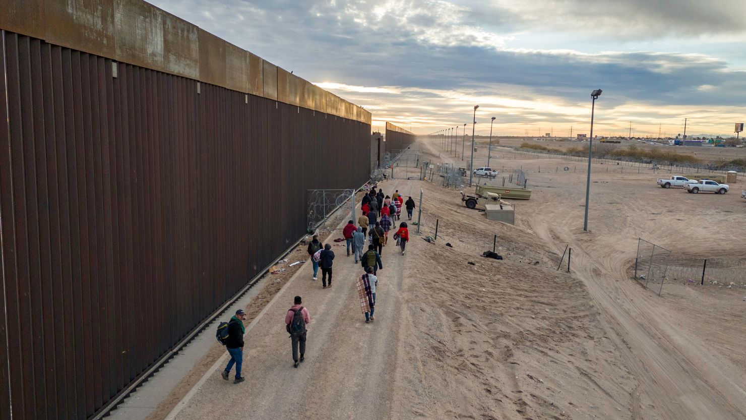 Migrants walk along the US-Mexico border wall after crossing the Rio Grande into El Paso, Texas, from Ciudad Juarez, Mexico, on February 1, 2024.