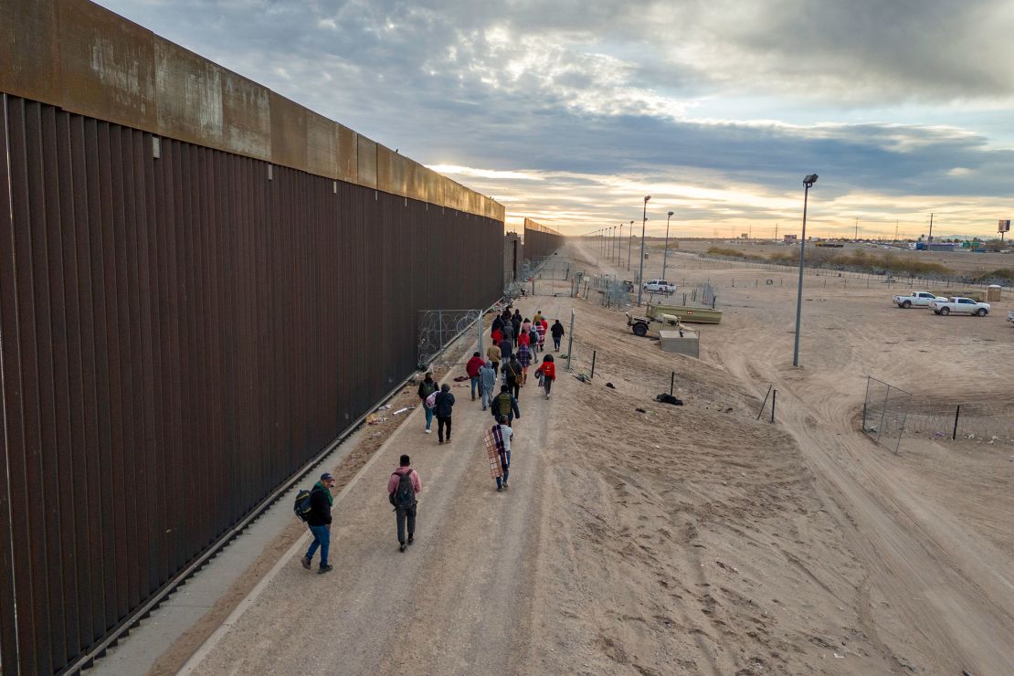 Immigrants walk along the U.S.-Mexico border wall after crossing the Rio Grande into El Paso, Texas on February 1, 2024.