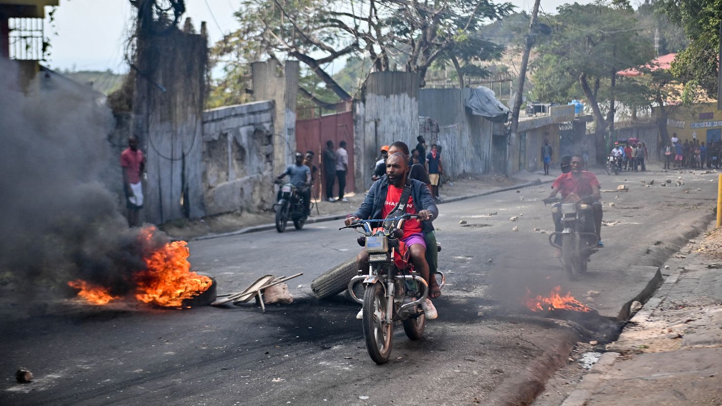 Motorcyclists pass burning tires during a demonstration calling for the resignation of Prime Minister Ariel Henry, in Port-au-Prince, Haiti, on February 6, 2024.