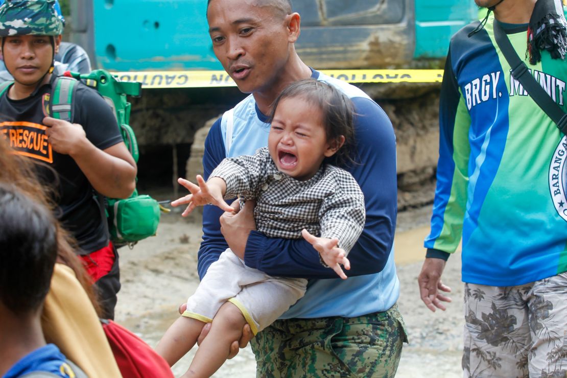 A policeman carries a baby as officials ordered mandatory evacuation from the landslide-hit village on February 8, 2024.