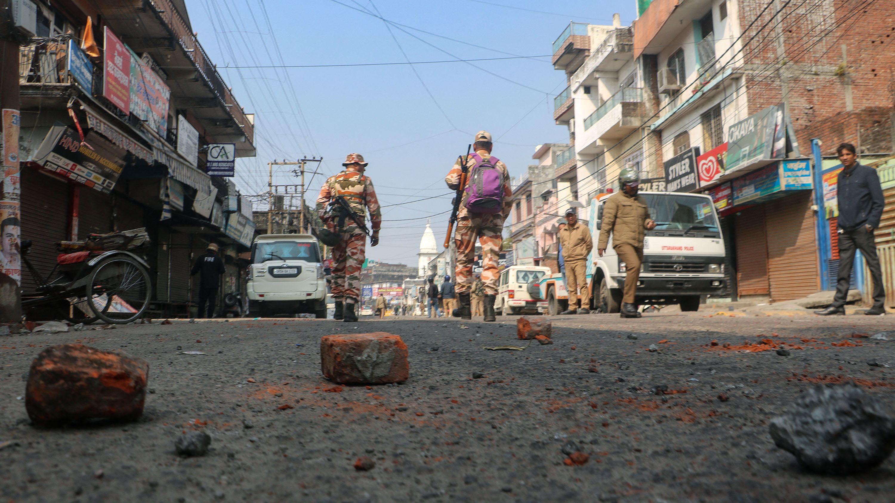 Security walk past bricks and stones scattered on a road after day an Islamic school in Haldwani was destroyed in Uttarakhand on February 9, 2024.