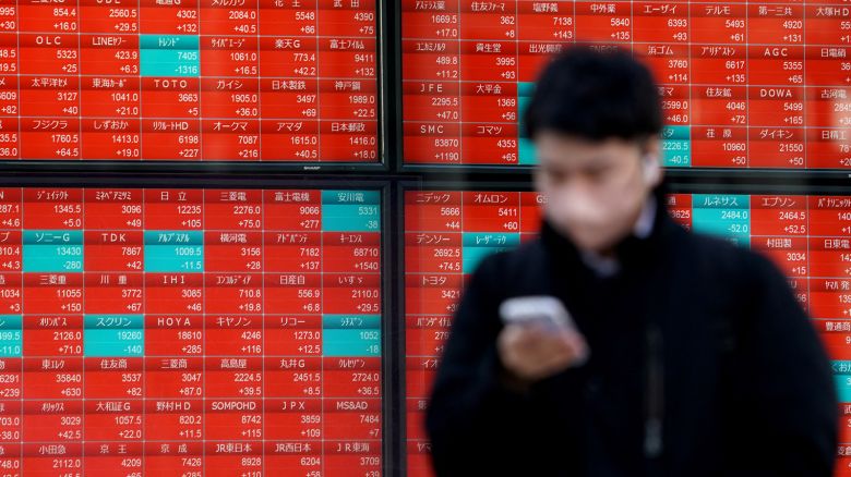 A man walks past an electronic board displaying stock prices of each company listed on the Tokyo Stock Exchange along a street in Tokyo on February 16, 2024.