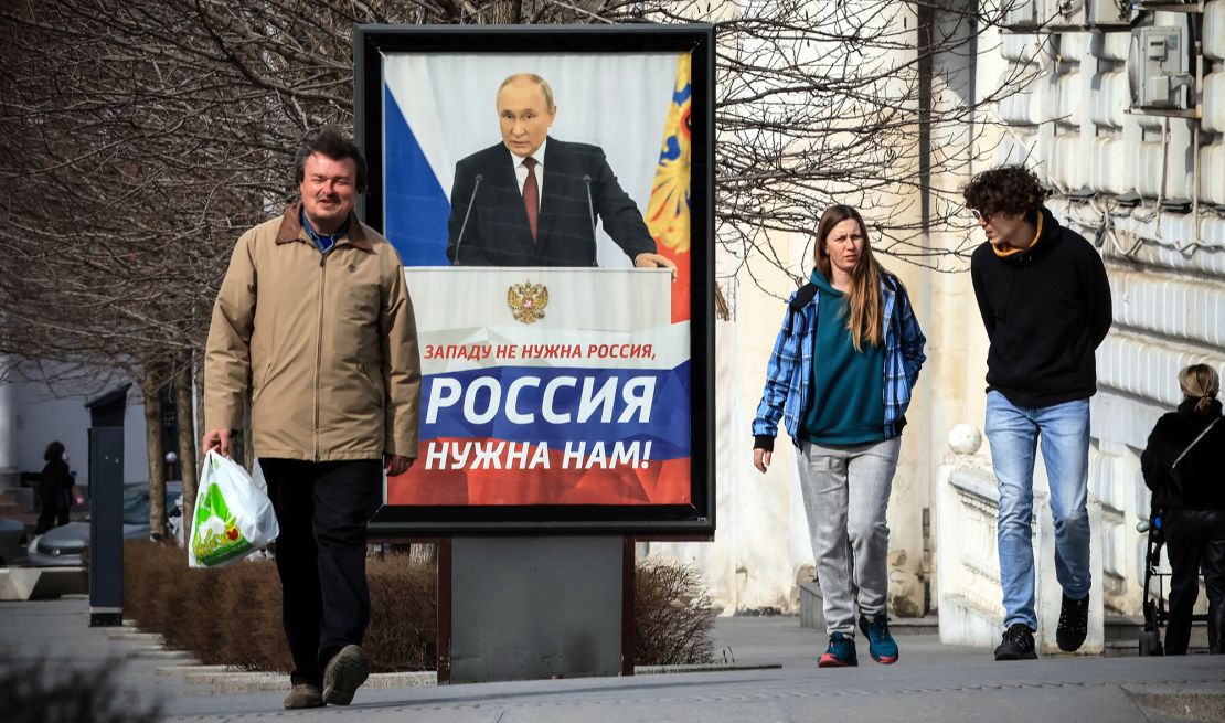 People walk in front of a poster showing Russian President Vladimir Putin and reading "The West doesn't need Russia. We need Russia!" in Simferopol, Crimea, on March 5, 2024.