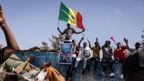TOPSHOT - A supporter of the coalition of anti-establishment candidates holds a Senegalese flag as they sit on top of a wall during a campaign rally in Dakar on March 10, 2024. Campaigning has got underway for Senegal's March 24 presidential election, after weeks of turmoil caused by its delay, and will largely take place during the Islamic fasting month of Ramadan in a country that is majority Muslim. (Photo by JOHN WESSELS / AFP) (Photo by JOHN WESSELS/AFP via Getty Images)
