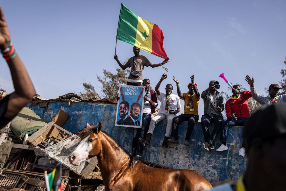 A supporter of the coalition of anti-establishment candidates holds a Senegalese flag as they sit on top of a wall during a campaign rally in Dakar on March 10, 2024.