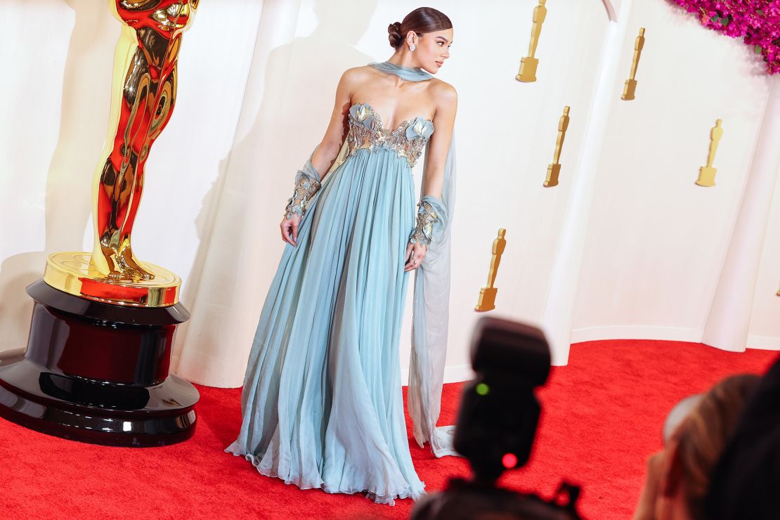 Hailee Steinfeld parecia um sonho em um vestido Elie Saab, com enfeites florais dourados no corpete e nos pulsos e um lenço no pescoço até o chão.