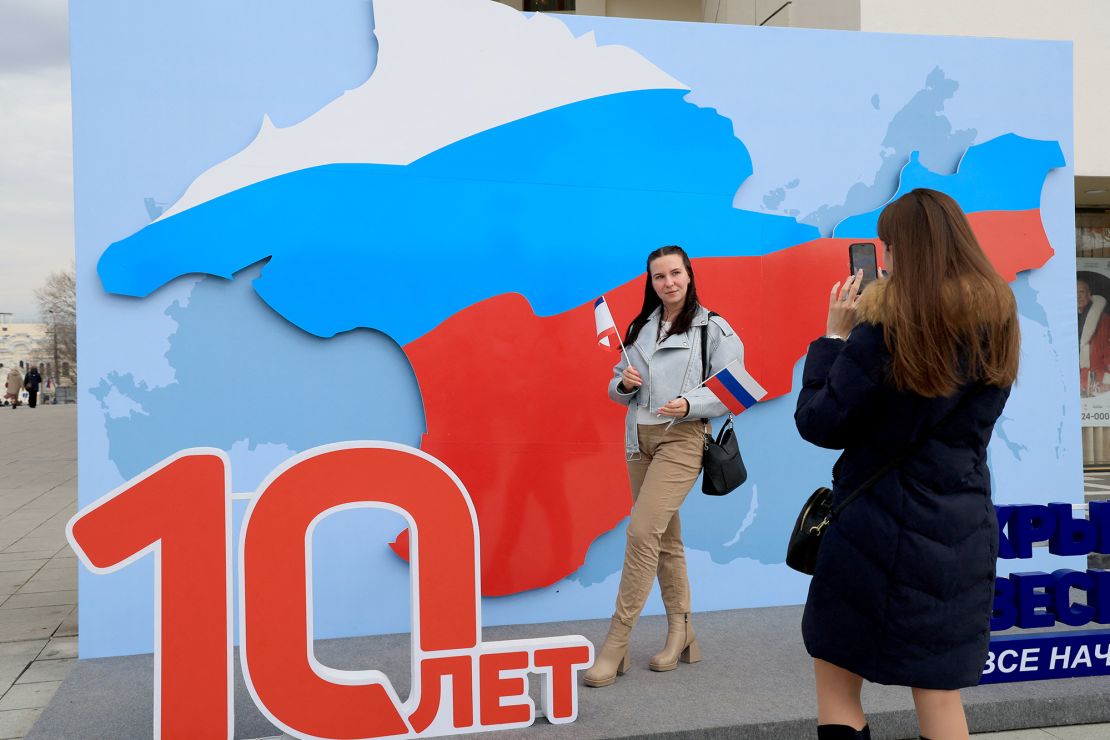 A woman poses for pictures with an artwork featuring the map of Crimea in the colours of the Russian flag, days before the 10th anniversary of Russia's annexation of Crimea, in Simferopol, March 13, 2024.