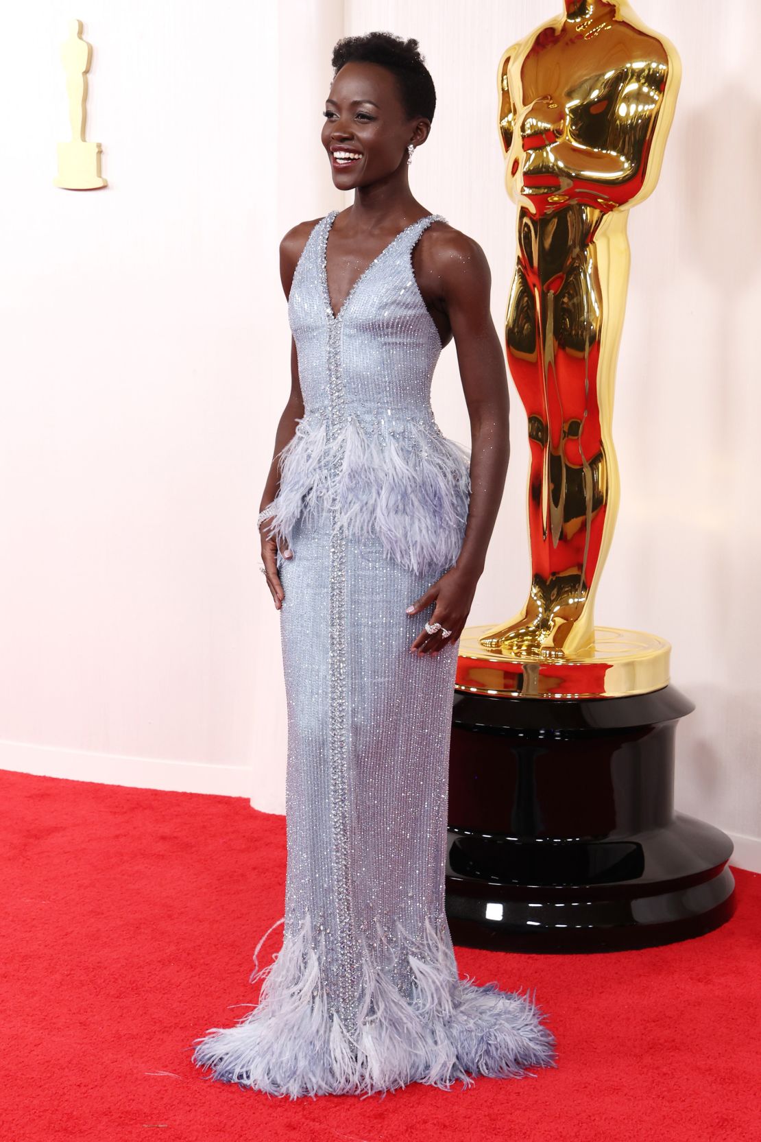Lupita Nyong'o hit the red carpet in a stunning Armani Privé dress with feather embellishments at the waist and hem.  The actor accessorized with white gold jewelry from De Beers.