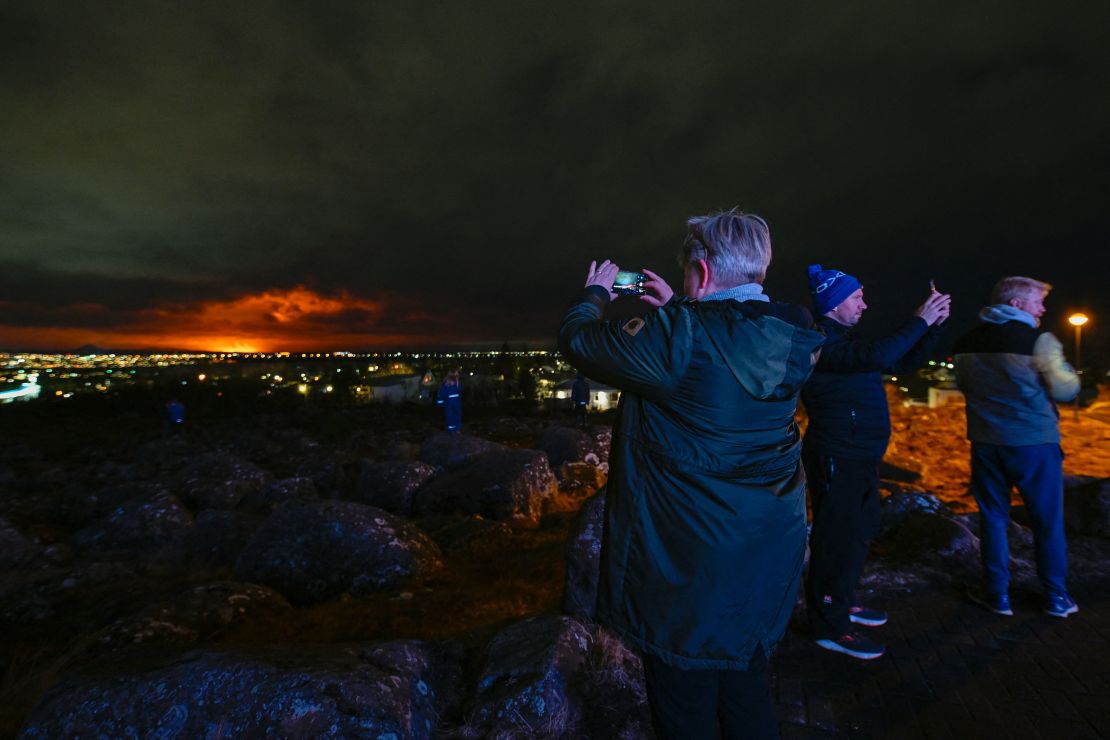 People on the outskirts of Reykjavik take pictures of the orange colored sky as molten lava flows out from a fissure on the Reykjanes peninsula north of the evacuated town of Grindavik, western Iceland, on March 16.