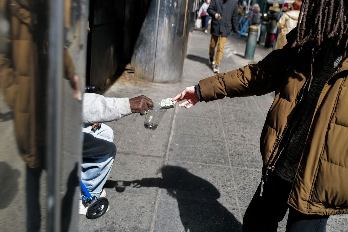 A pedestrian gives a dollar bill to a homeless man March 19 in New York.