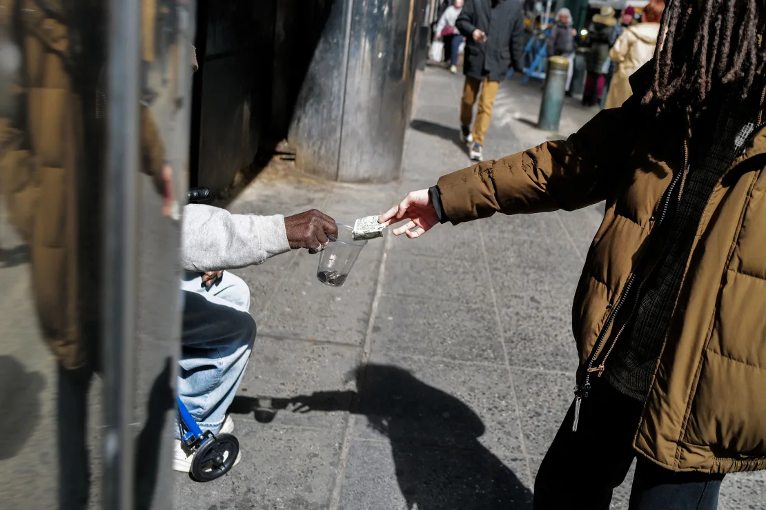 A pedestrian gives a dollar bill to a⁣ homeless man March 19 in New York.