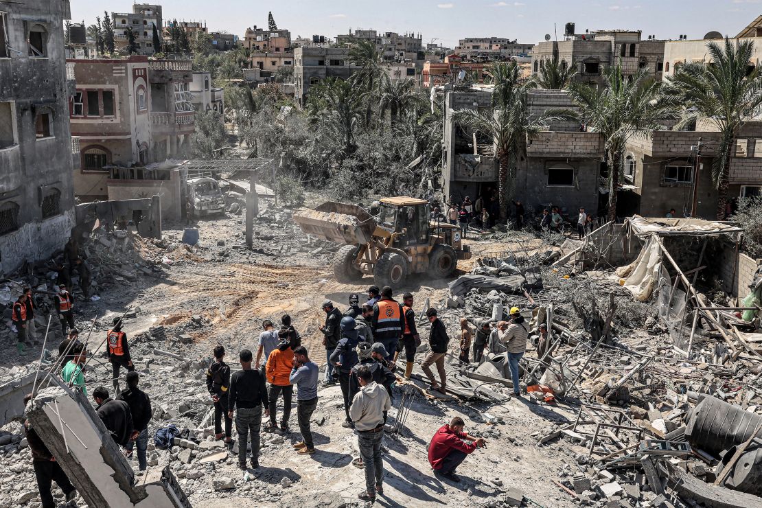 An excavator clears debris as people and first responders inspect the rubble of a building that collapsed following an Israeli air strike in the Rafah refugee camp in the southern Gaza Strip on March 20, 2024 amid the ongoing conflict in the Palestinian territory between Israel and the militant group Hamas. (Photo by SAID KHATIB / AFP) (Photo by SAID KHATIB/AFP via Getty Images)