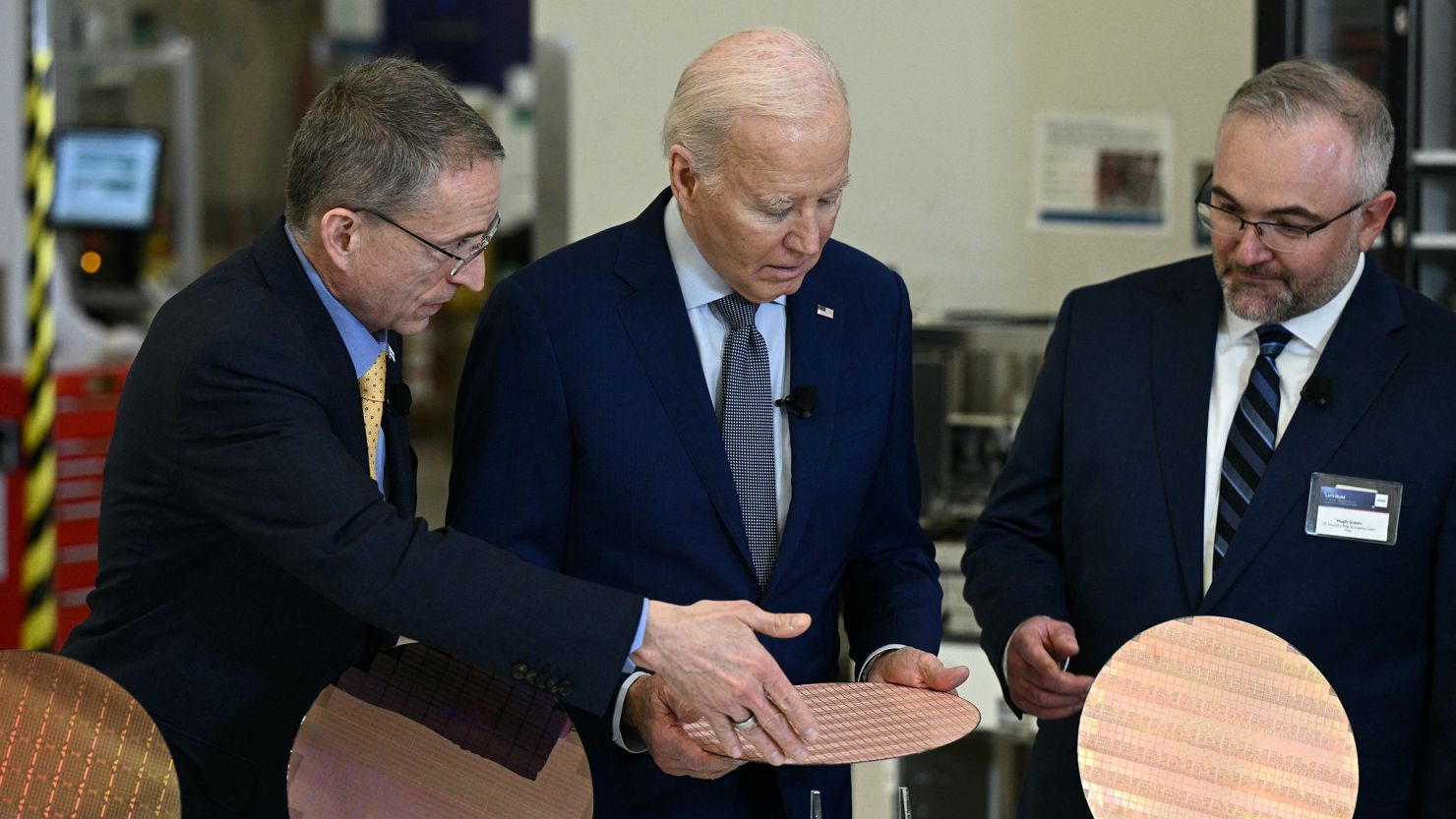 President Joe Biden, center, stands behind a table, next to Intel's CEO Pat Gelsinger, left, as they look at wafers of chips while touring the Intel Ocotillo Campus in Chandler, Arizona, on March 20.