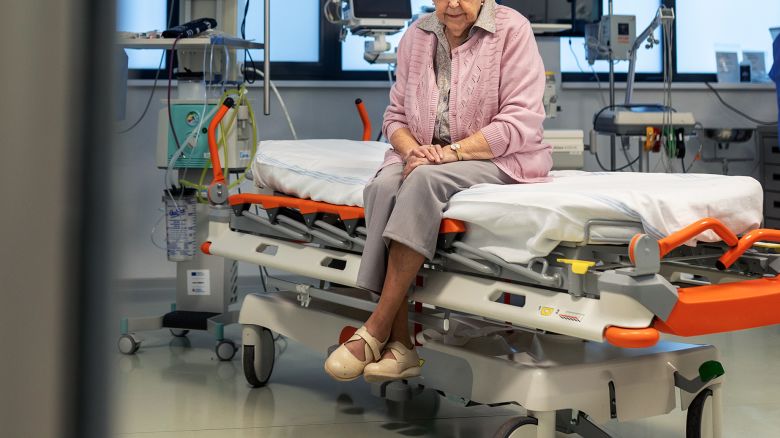 Senior patient sitting on examination table in hospital emergency room, waiting for doctor.