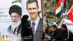 Portraits of Syria's President Bashar al-Assad (R) and Iran's supreme leader Ayatollah Ali Khamenei stand as Palestinians sit at the entrance of the Yarmuk camp for Palestinian refugees, south of Damascus, during a delivery of humanitarian aid provided by Iran as part of the Muslim holy fasting month of Ramadan on March 26, 2024. (Photo by LOUAI BESHARA / AFP) (Photo by LOUAI BESHARA/AFP via Getty Images)