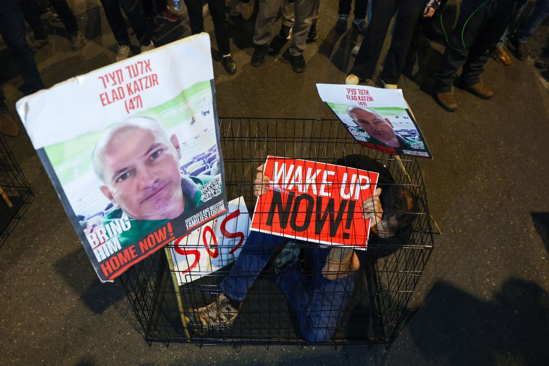 A man sits in a cage with portraits of 47-year-old Israeli hostage Elad Katzir, in Tel Aviv, Israel on March 26, 2024.