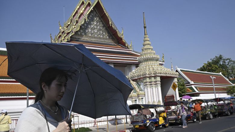 TOPSHOT - Tourists shield themselves from the sun with umbrellas to combat the heat outside of Wat Pho Buddhist temple in Bangkok on April 1, 2024. (Photo by Lillian SUWANRUMPHA / AFP) (Photo by LILLIAN SUWANRUMPHA/AFP via Getty Images)