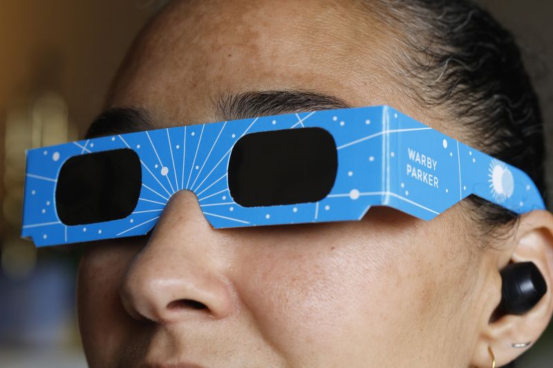 In this photo illustration, a woman models eclipse glasses from Warby Parker on April 01, 2024 in New York City. Warby Parker announced that it will be offering free glasses certified for safe viewing of the upcoming solar eclipse on April 8. People can visit any store to receive up to two pairs of solar eclipse glasses at no cost. The event will mark the last total solar eclipse that is visible from the United States until 2044.