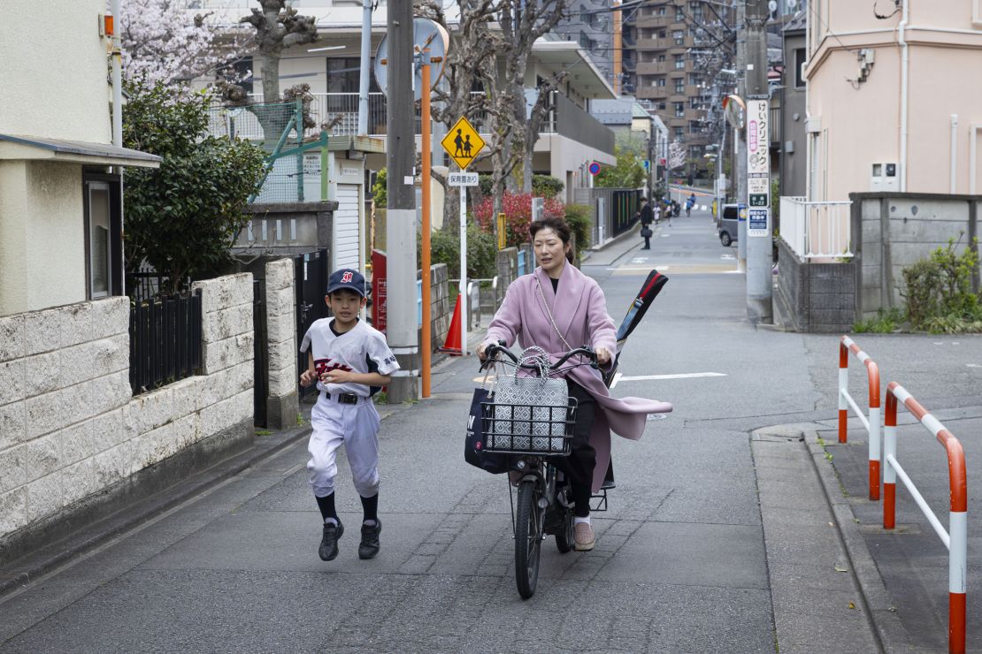 TOKYO, JAPAN - 2024/04/06: Son dressed in baseball attire runs along with his mom riding a bicycle while carrying his baseball bat. (Photo by Stanislav Kogiku/SOPA Images/LightRocket via Getty Images)