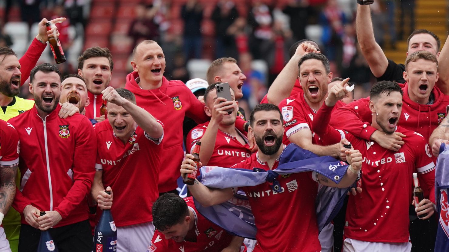 Wrexham players on the pitch celebrating promotion to League One after the final whistle.