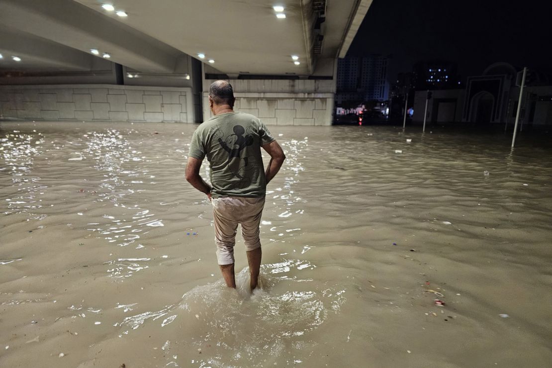 On Tuesday, individuals are seen wading through a flooded street under a bridge in the United Arab Emirates after a heavy rainfall.