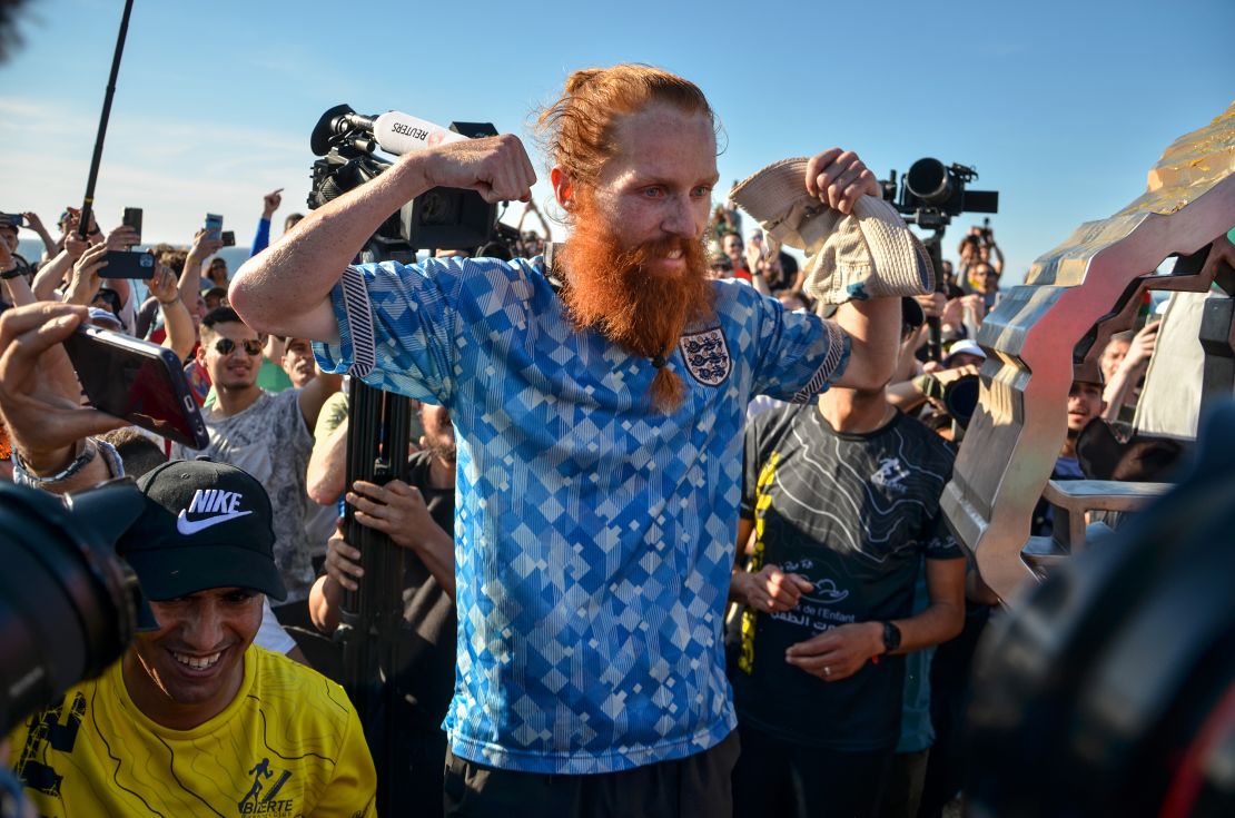 British runner Russ Cook gestures as he poses for a picture with the memorial sign marking the northern-most point of Africa upon arrival at Cape Angela, northeast of Tunis, on April 7, 2024 while surrounded by supporters who joined him for the final leg of the 16,000 kilometer challenge to run across the African continent from South Africa's Cape Agulhas to Tunisia's Cape Angela to raise money for charity. (Photo by Hasan Mrad/UCG/Universal Images Group via Getty Images)