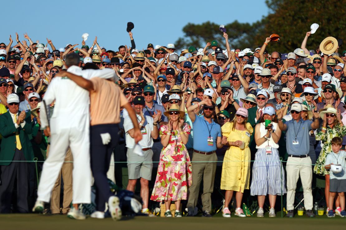 Patrons cheer as Scottie Scheffler and his caddie, Ted Scott, celebrate on the 18th green after winning the Masters.