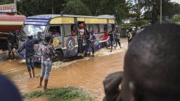 Pedestrians hang off the sides of a matatu (public transport bus)as it drives across a flooded section of road after a stream burst it's banks overnight following heavy seasonal rain in the capital, Nairobi on April 24, 2024. Storms and flash floods wreaked devastation across the Kenyan capital Nairobi on April 24, 2024, claiming at least four lives. (Photo by Tony KARUMBA / AFP) (Photo by TONY KARUMBA/AFP via Getty Images)