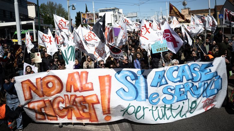 Protestors hold a banner reading "No to ticket, Yes to houses and services for all" as they take part in a demonstration, against the new "Venice Access Fee", organised by the list "Tutta la citta' insieme" (The whole city together) and members of several Venetians trade associations in "Piazzale Roma" in Venice, on April 25, 2024. Venice launched a new scheme to charge day-trippers for entering the historic Italian city, a world first intended to ease the pressure of mass tourism , but many residents are opposed, in Venice, on April 25, 2024. (Photo by MARCO BERTORELLO / AFP) (Photo by MARCO BERTORELLO/AFP via Getty Images)