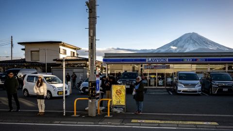 This photo taken on January 1, 2024 shows tourists posing in front of a convenience store with Mount Fuji in the background, in the town of Fujikawaguchiko, Yamanashi prefecture. A huge black barrier to block Mount Fuji from view will be installed in a popular photo spot by Japanese authorities exasperated by crowds of badly behaved foreign tourists, it was reported on April 26, 2024. (Photo by Philip FONG / AFP) (Photo by PHILIP FONG/AFP via Getty Images)