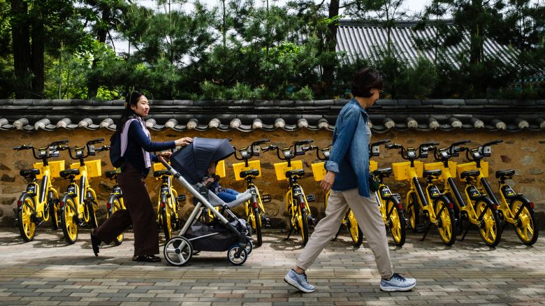 A woman pushes her child in a stroller past rental bicycles in Seoul on April 26, 2024.
