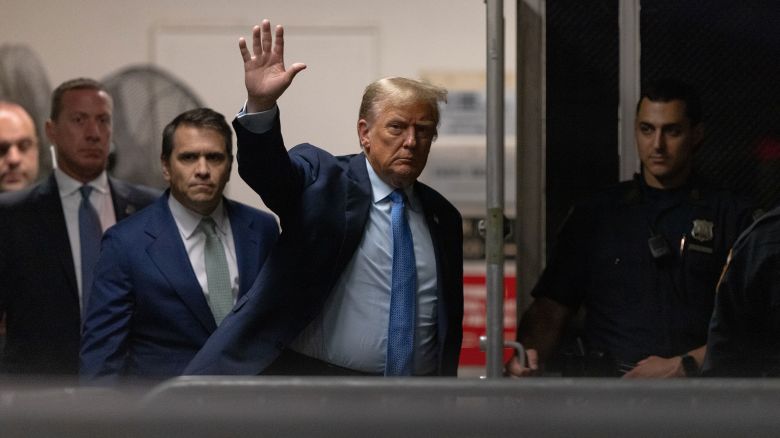Donald Trump waves while walking through a dark hallway