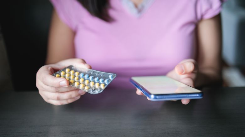 Unrecognizable woman holding her contraceptives birth control pills and mobile phone with health plan to prevent pregnancy.