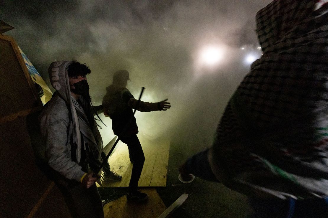 Pro-Palestinian demonstrators engulfed in tear gas regroup and rebuild the barricade surrounding the encampment set up on the campus of the University of California Los Angeles (UCLA) as clashes erupt with counter protesters, in Los Angeles on May 1, 2024.