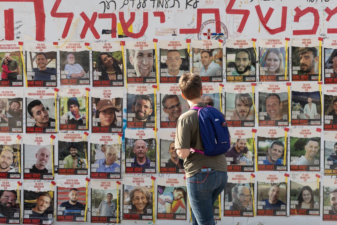 A woman looks at a wall, which is covered in photographs of people. 