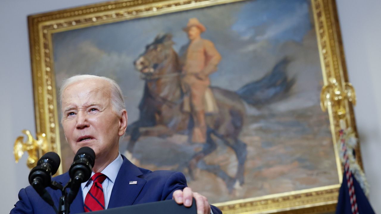 American President Joe Biden speaks at a podium. Over his shoulder is a painting of former American President Teddy Roosevelt.