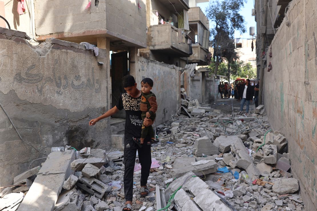 A Palestinian youth carries a child as he walks through rubble in Rafah's Tal al-Sultan district on Tuesday.