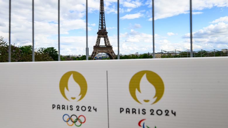 06 May 2024, France, Paris: The Olympic rings and the Paralympic Games logo can be seen on a sign on a construction fence in front of the Eiffel Tower. The Olympic Games and Paralympics take place in France this summer.
