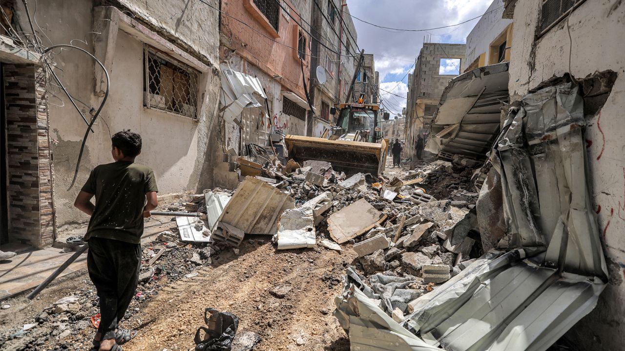 TOPSHOT - A boy walks before a bulldozer clearing rubble along a heavily-damaged street in the Tulkarem camp for Palestinian refugees, after an Israeli military raid there, in the north of the occupied West Bank on May 7, 2024. (Photo by JAAFAR ASHTIYEH / AFP) (Photo by JAAFAR ASHTIYEH/AFP via Getty Images)