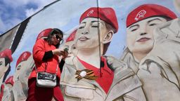 TOPSHOT - A woman uses her smartphone walking past a mural depicting members of Russia's Young Army patriotic movement in Moscow on May 14, 2024.