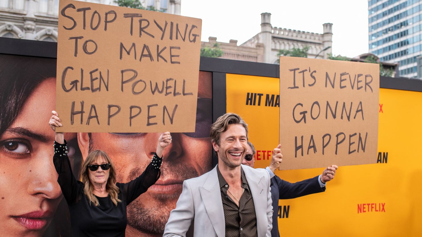 Glen Powell's parents hold up signs behind him as they attend the special screening of "Hitman" in Austin, Texas on Wednesday.