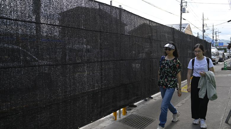 People walk pass the black screen as the city of Fujikawaguchiko built a screen to dissuade tourists from taking photos of Mount Fuji, Japan's most famous heritage, from a sidewalk in front of a Lawson convenience store on May 21, 2024, at Fujikawaguchiko city in Yamanashi Prefecture, Japan.