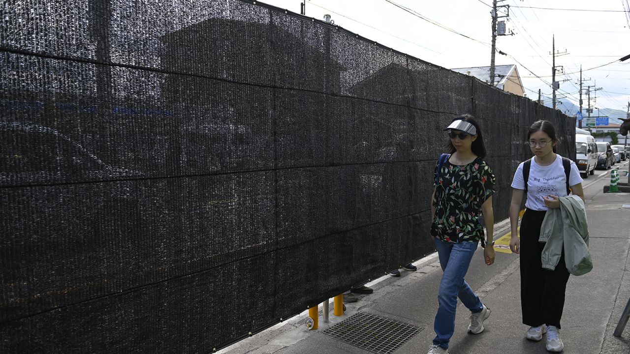 People walk pass the black screen as the city of Fujikawaguchiko built a screen to dissuade tourists from taking photos of Mount Fuji, Japan's most famous heritage, from a sidewalk in front of a Lawson convenience store on May 21, 2024, at Fujikawaguchiko city in Yamanashi Prefecture, Japan.