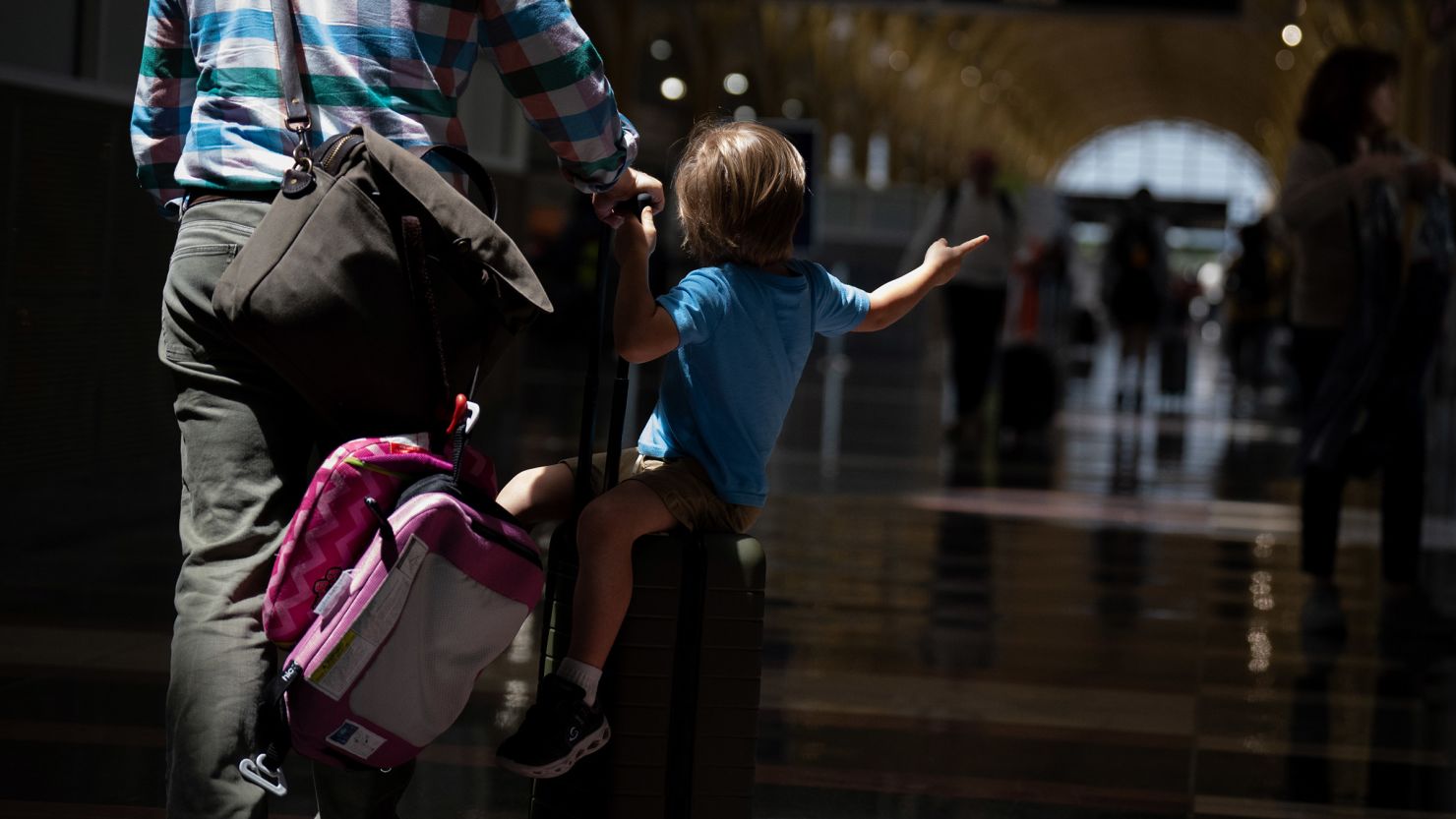 A boy sits on a rolling suitcase as travelers make their way through Ronald Reagan Washington National Airport in Arlington, Virginia on May 24, 2024.