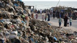 People walk by piles of trash in Deir al Balah, Gaza on May 26.